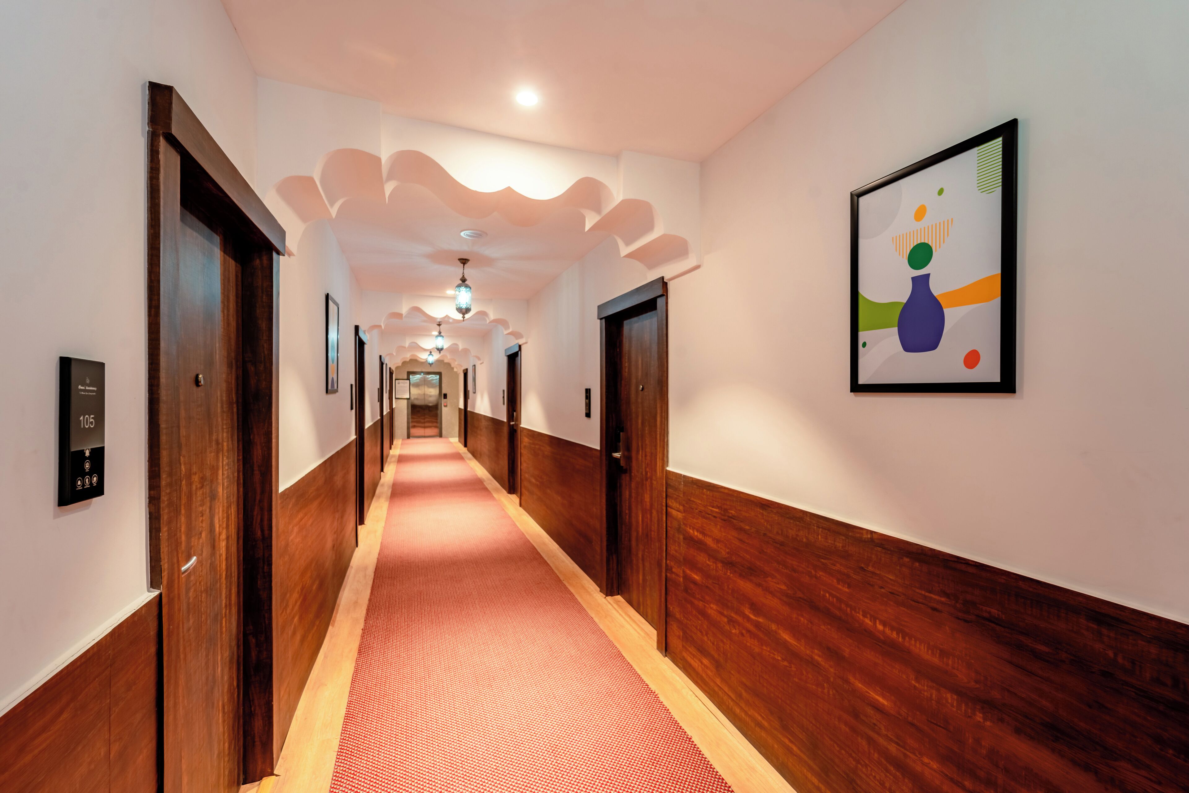 Een hotelgangen met houten deuren, een roodgekleurd tapijt en een plafond met een bijzonder ontwerp.