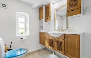 Een badkamer met een witte wastafel, houten kastjes, een spiegel en een raam.