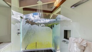 A modern shower with a glass enclosure, a built-in bench, and a view of a mountainous landscape. - Kolohala in Haena is a tranquil place to enjoy your tropical vacation! (Haena)