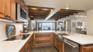 A modern kitchen with wooden cabinets, a central island, and a view of a snowy landscape. - Ski in/Out 7th Floor Penthouse at Purg - Huge Deck w/ Mountain/Slope Views/AC (Durango)