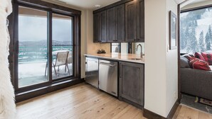 A modern kitchen with dark wooden cabinets, a stainless steel refrigerator, and a large window overlooking a snowy landscape. - Ski in/Out 7th Floor Penthouse at Purg - Huge Deck w/ Mountain/Slope Views/AC (Durango)