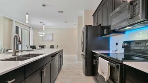 Una cocina moderna con una isla grande, electrodomésticos de acero inoxidable e iluminación colgante.
