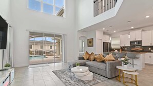 Ein geräumiger Wohnbereich mit grauem Sofa, einem Couchtisch und einem Fernseher. Ein Balkon mit Blick auf den Pool ist vorhanden.