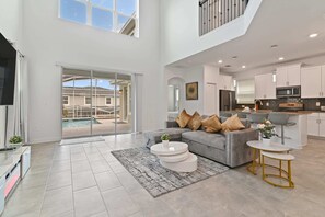 A spacious living area with a grey sofa, a coffee table, and a TV. There is a balcony with a pool view.