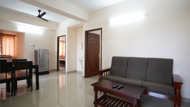 A living room with a sofa, a wooden coffee table, and a dining area with a table and chairs. - Aishwaryam Service Apartment (Chennai)