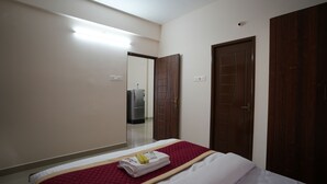 A hotel room with a bed, a wooden door, a mirror, and a hallway leading to a kitchen area. - Aishwaryam Service Apartment (Chennai)