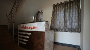 A reception desk with a sign reading "Dishwaryam" in a hotel lobby with a staircase and patterned curtains. - Aishwaryam Service Apartment (Chennai)