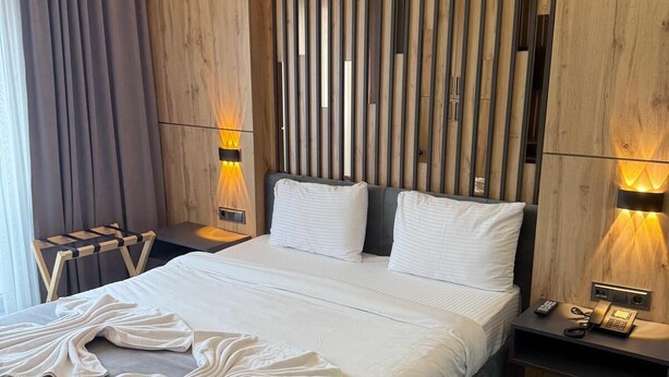 Una habitación de hotel moderna con cabecera de madera, una cama grande con ropa blanca, dos lámparas de noche y suelo de madera.