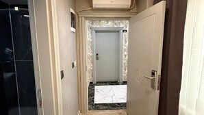Un pasillo con suelo de mármol, una puerta de cristal a la izquierda y otra puerta con placa de número al final.