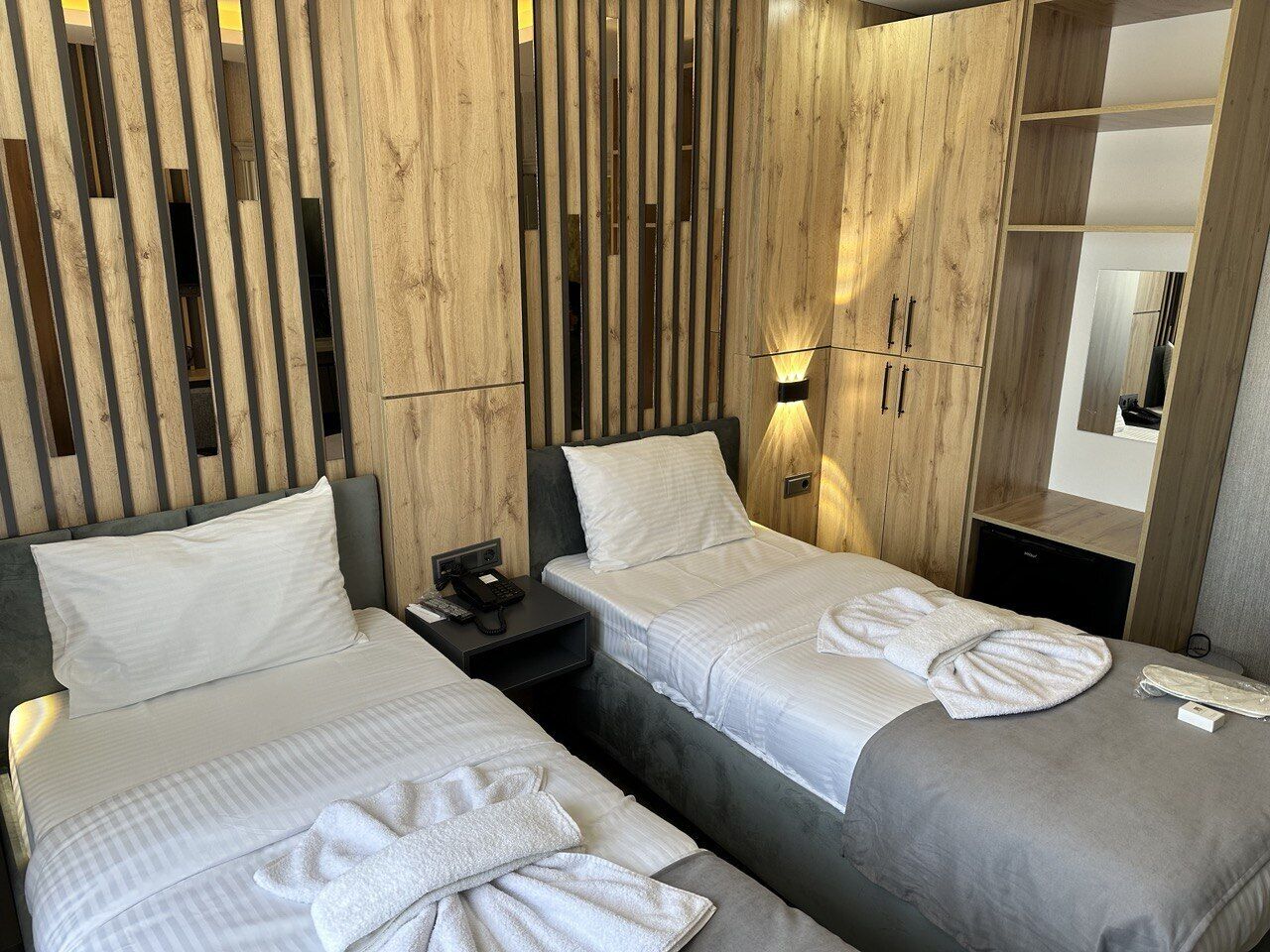 Una habitación de hotel con dos camas, cabecero de madera, mesita de noche y un espejo.