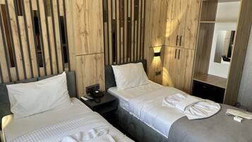 Una habitación de hotel con dos camas, cabecero de madera, mesita de noche y un espejo.