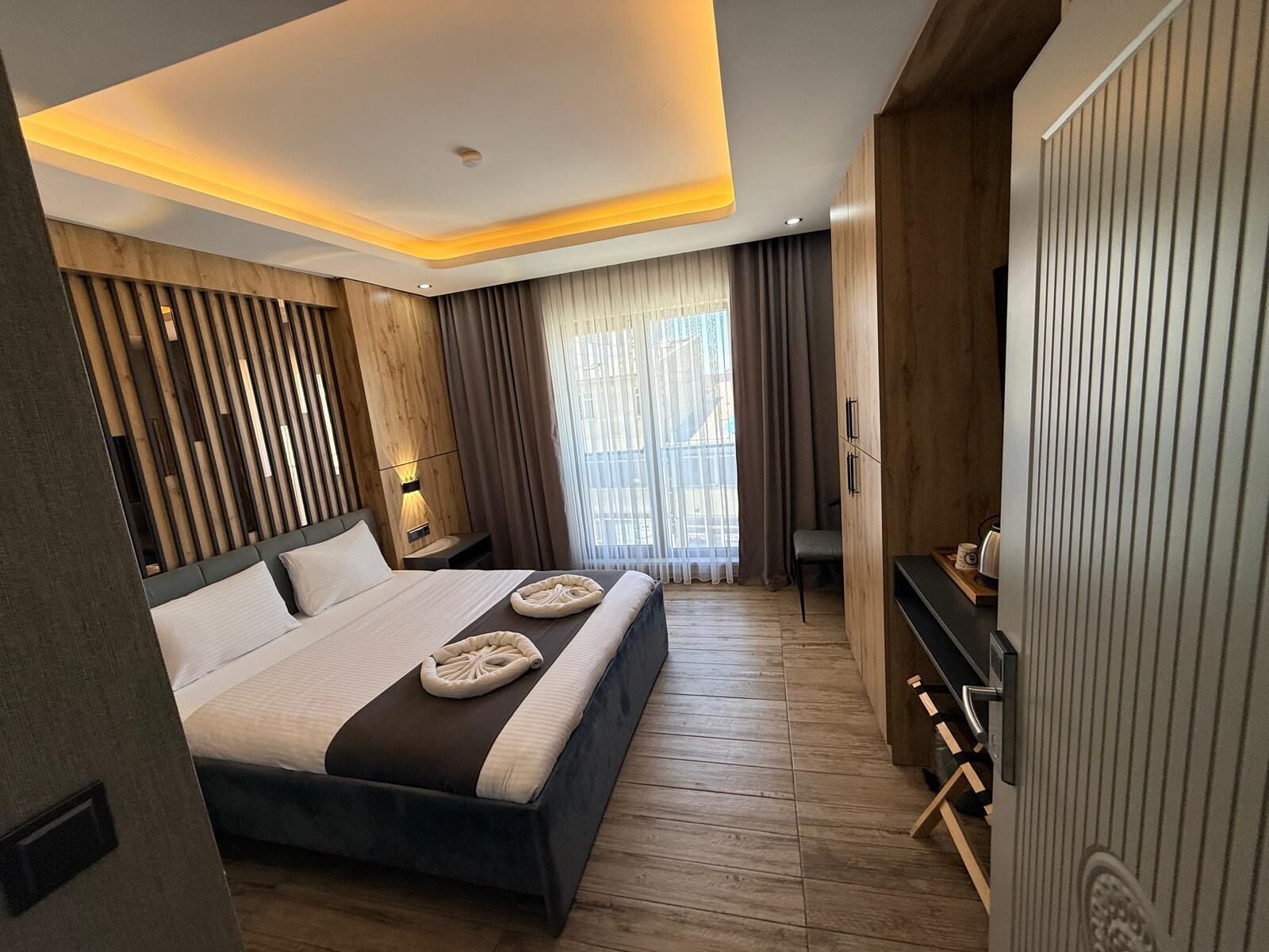 Un dormitorio moderno con una cama grande, paneles de madera, un escritorio y vistas al exterior.