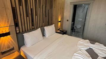 Une chambre d’hôtel moderne avec un grand lit, un mur lambrissé en bois et une salle de bain visible à travers une porte en verre.