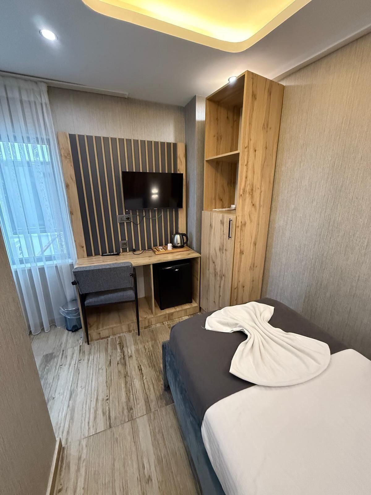 A modern hotel room with a bed, a desk, a TV, and a wardrobe.