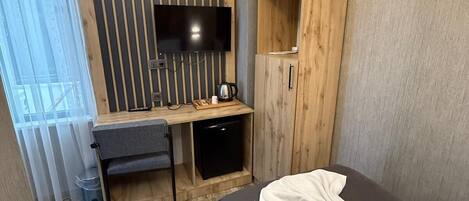 A modern hotel room with a bed, a desk, a TV, and a wardrobe.