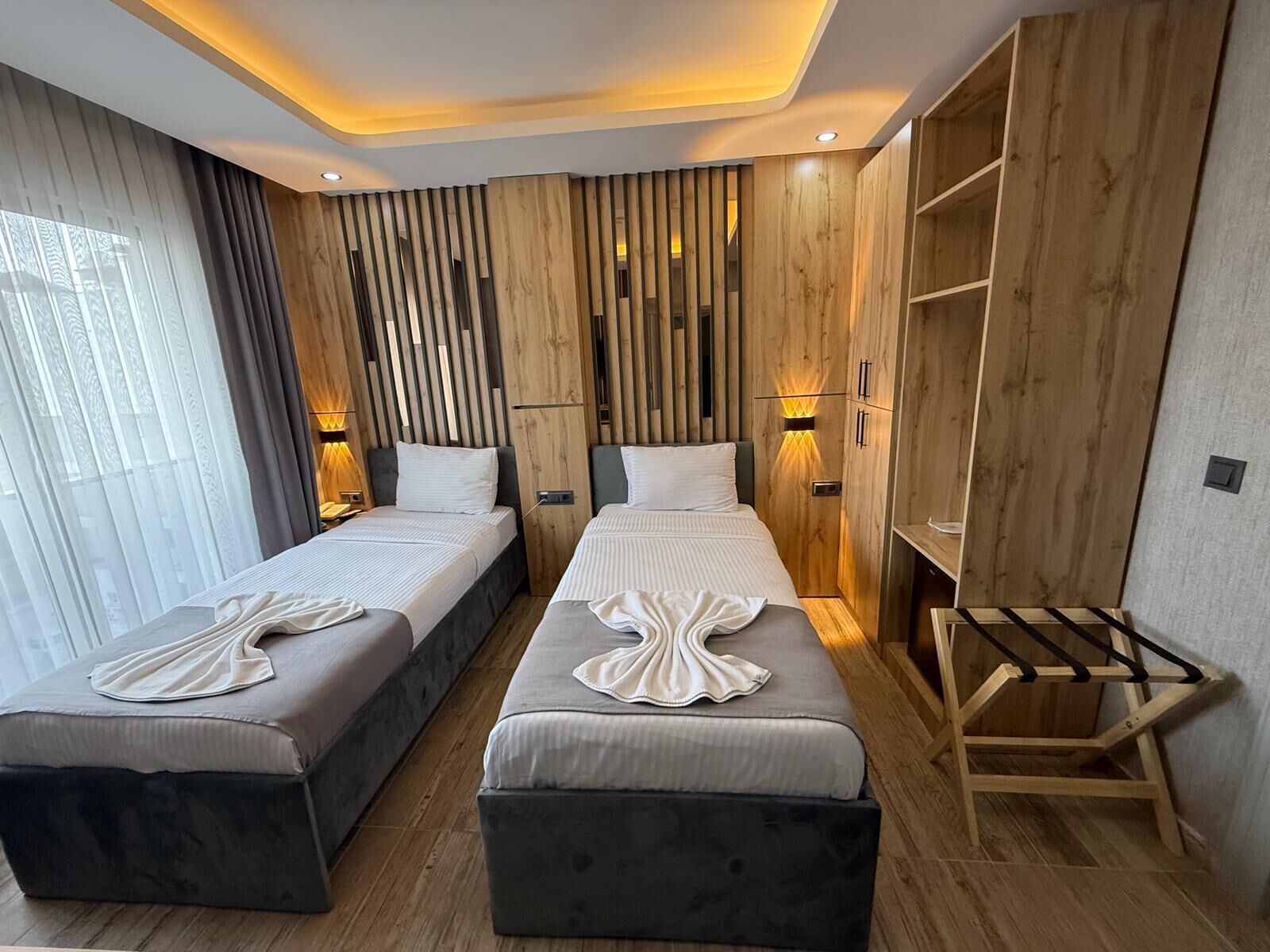A modern hotel room with two beds, wooden paneling, and built-in shelves.