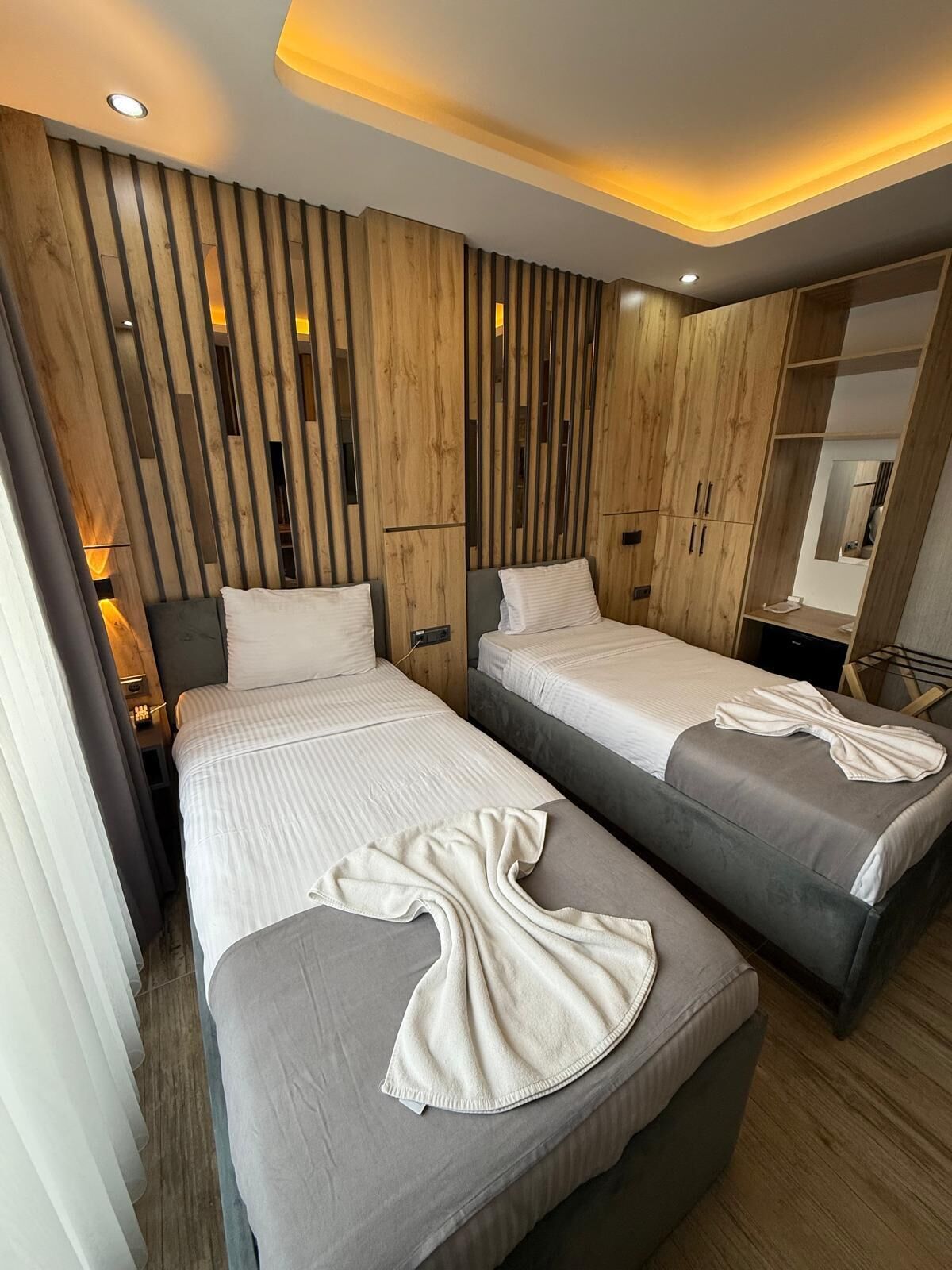 A modern hotel room with two beds, wooden paneling on the walls, and a mirror above the beds.
