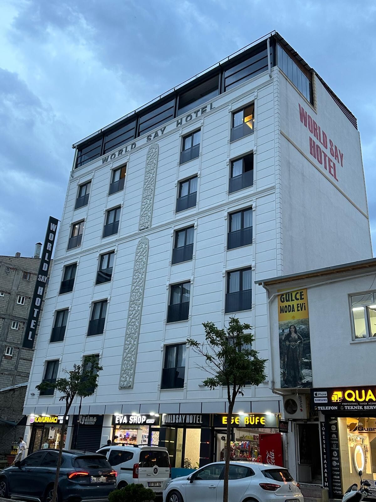A multi-story hotel with a prominent 'WORLD SAY HOTEL' sign, several ground-level shops, and parked cars.