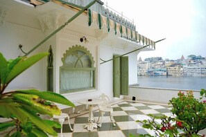 A balcony with a checkered floor, a white chair, and a view of a cityscape. - Hotel Amet Haveli (Udaipur)
