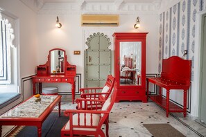 A room with a red vanity, a mirror, a red bench, and a red table with a vase. - Hotel Amet Haveli (Udaipur)