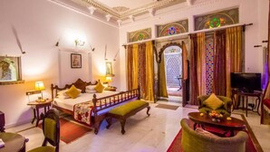 A hotel room with a bed, a bench, a sofa, a television, and a dining table. - Hotel Amet Haveli (Udaipur)