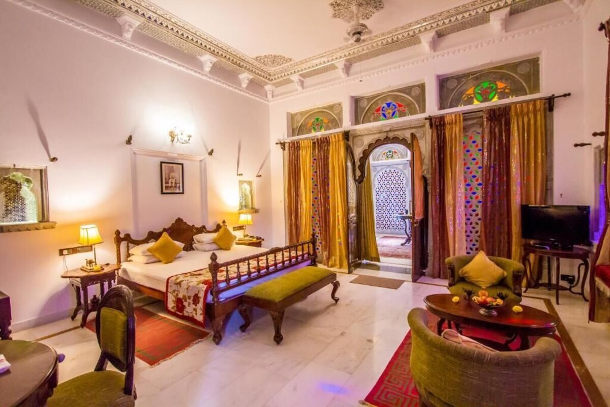 A hotel room with a bed, a bench, a sofa, a television, and a dining table.