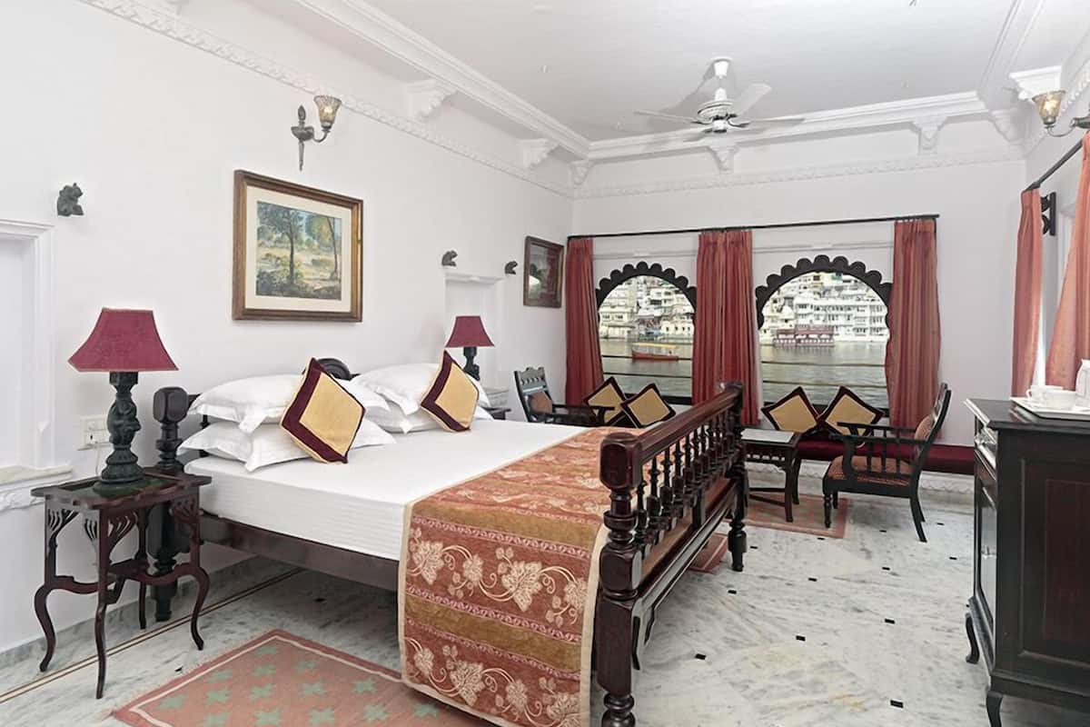 A hotel room with a large bed, a desk, a chair, and a view of a cityscape through a window.