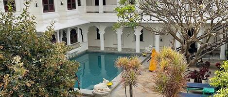 Un patio con piscina, mobiliario exterior y un edificio blanco con arcos.