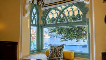 Ein Zimmer mit Erkerfenster und Blick auf ein Gewässer, ein Tisch mit Stuhl und eine gepolsterte Bank.