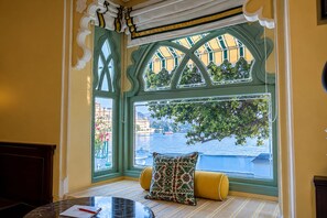 A room with a bay window overlooking a body of water, a table with a chair, and a cushioned bench. - Hotel Amet Haveli (Udaipur)