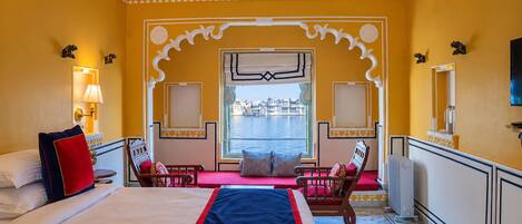 A hotel room with a large bed, a view of a body of water, and traditional decor.