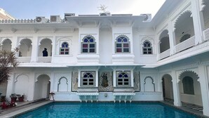 A traditional building with a central pool, arched windows, and white ornate detailing. - Hotel Amet Haveli (Udaipur)