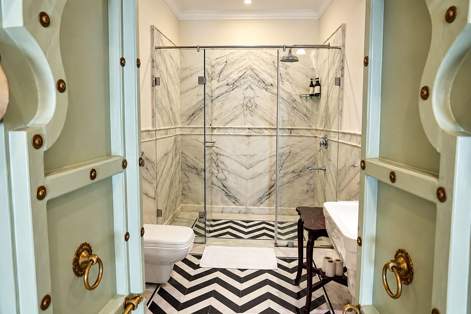 A bathroom with a shower, toilet, and sink, featuring marble walls and a chevron-patterned floor.