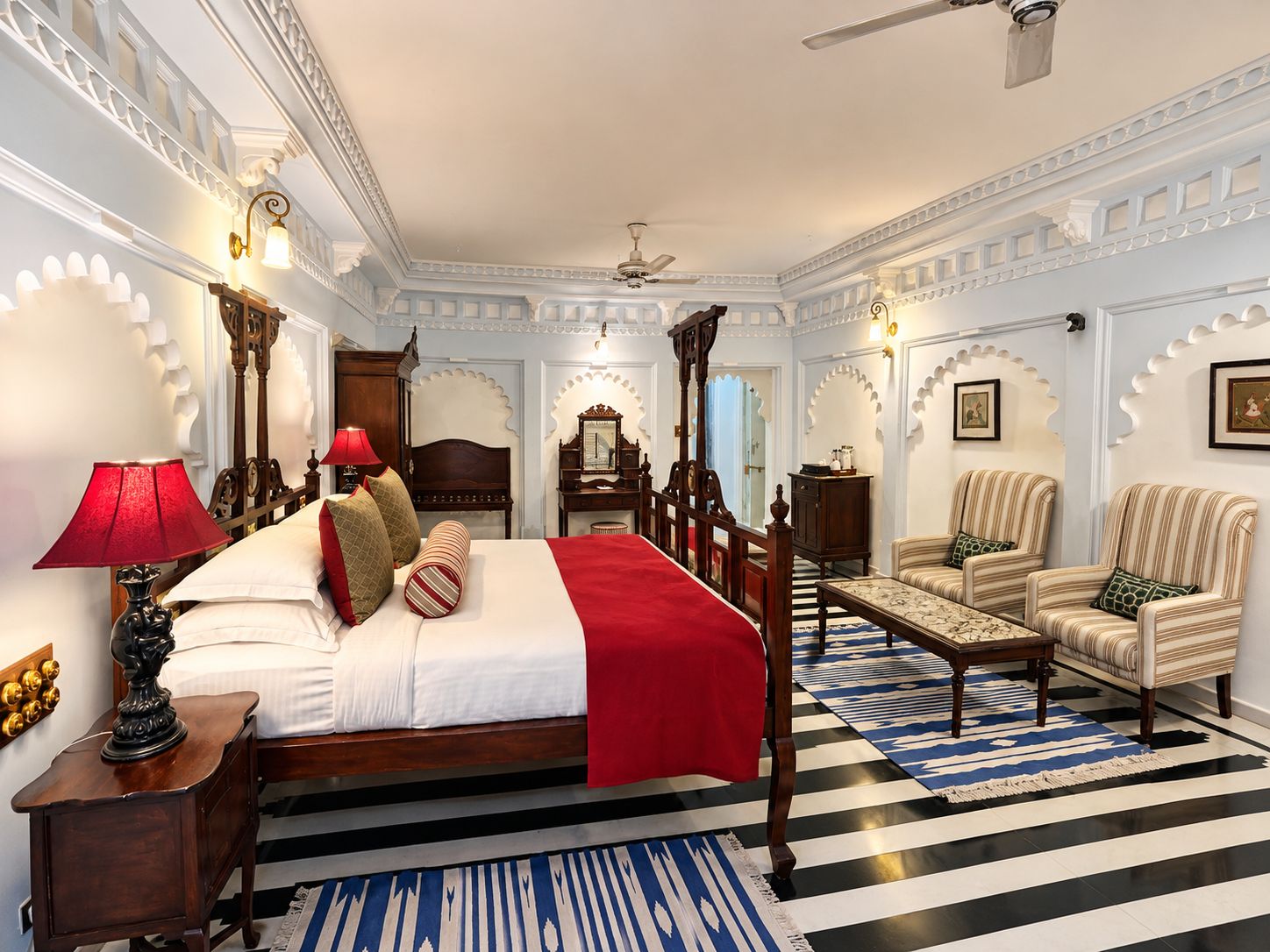 Een hotelkamer met een groot bed, een zithoek met stoelen, een bureau en een plafondventilator.