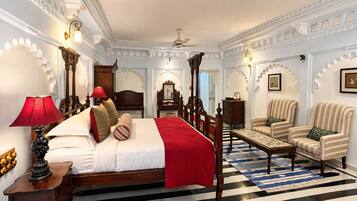 Een hotelkamer met een groot bed, een zithoek met stoelen, een bureau en een plafondventilator.