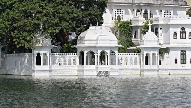 A white building with domed structures and arched windows, situated by a body of water. - Hotel Amet Haveli (Udaipur)