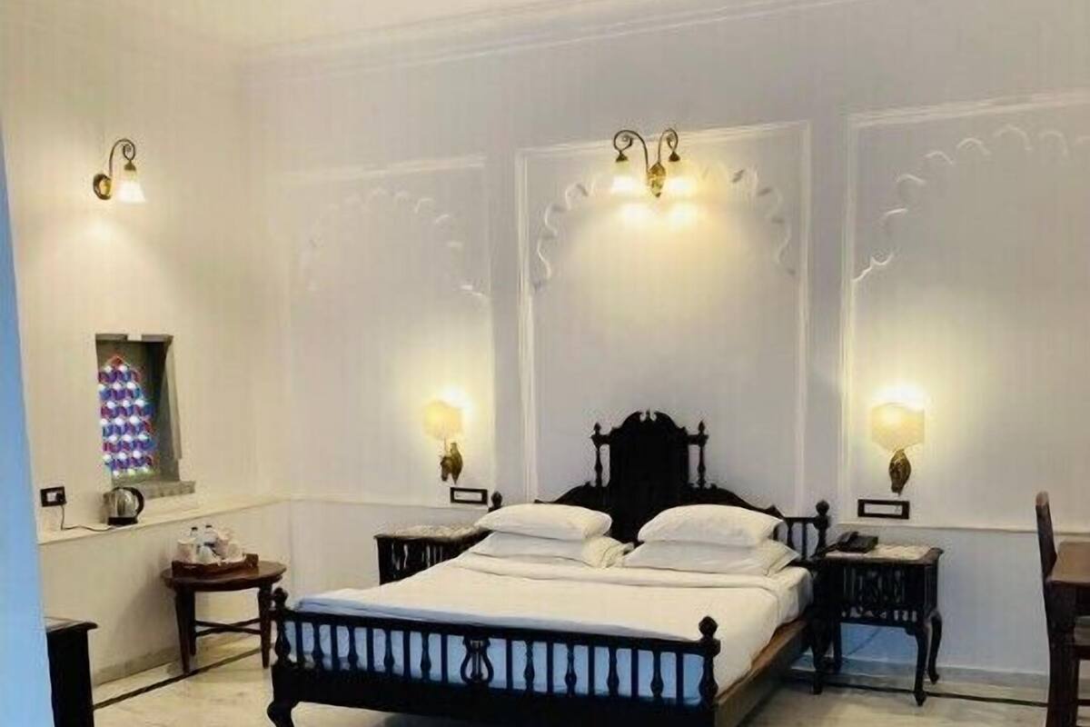 A bedroom with a four-poster bed, two bedside tables, a small window, and decorative wall sconces.