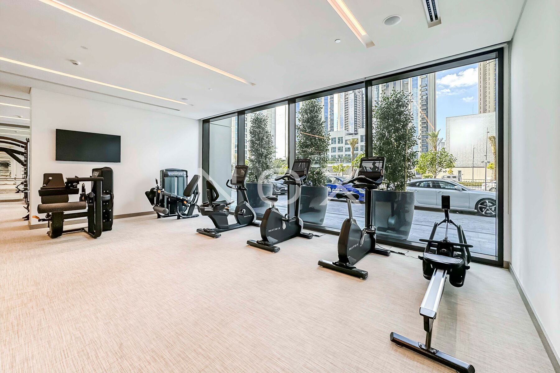 A modern gym with various exercise equipment, large windows, and a view of the city.