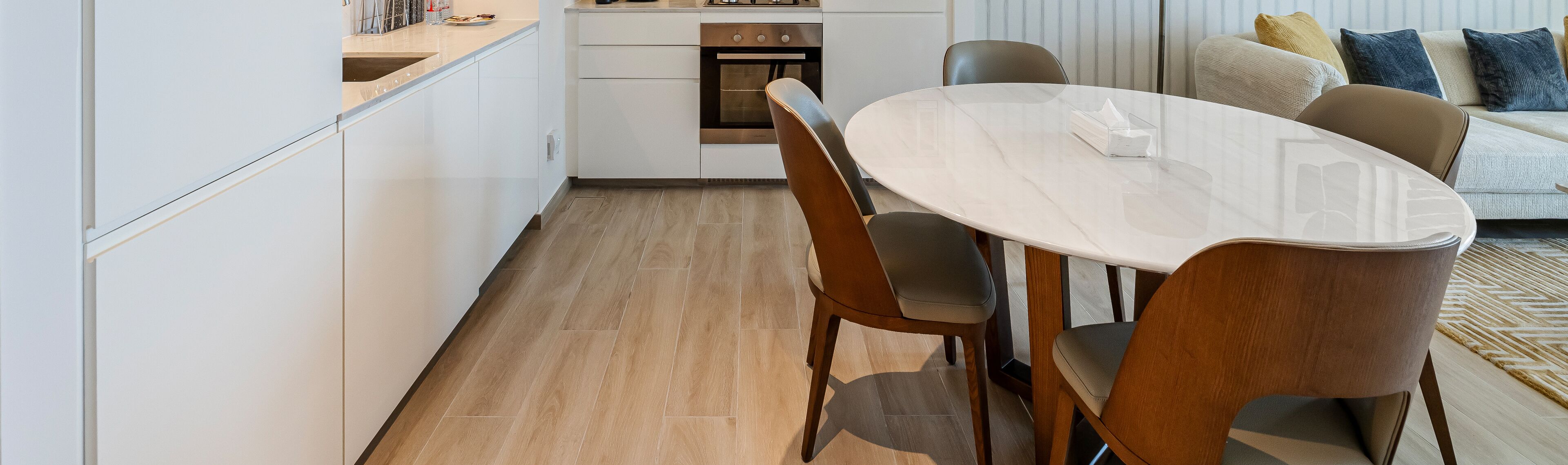 A modern kitchen with white cabinets, a built-in oven, and a dining area with a round table and chairs.