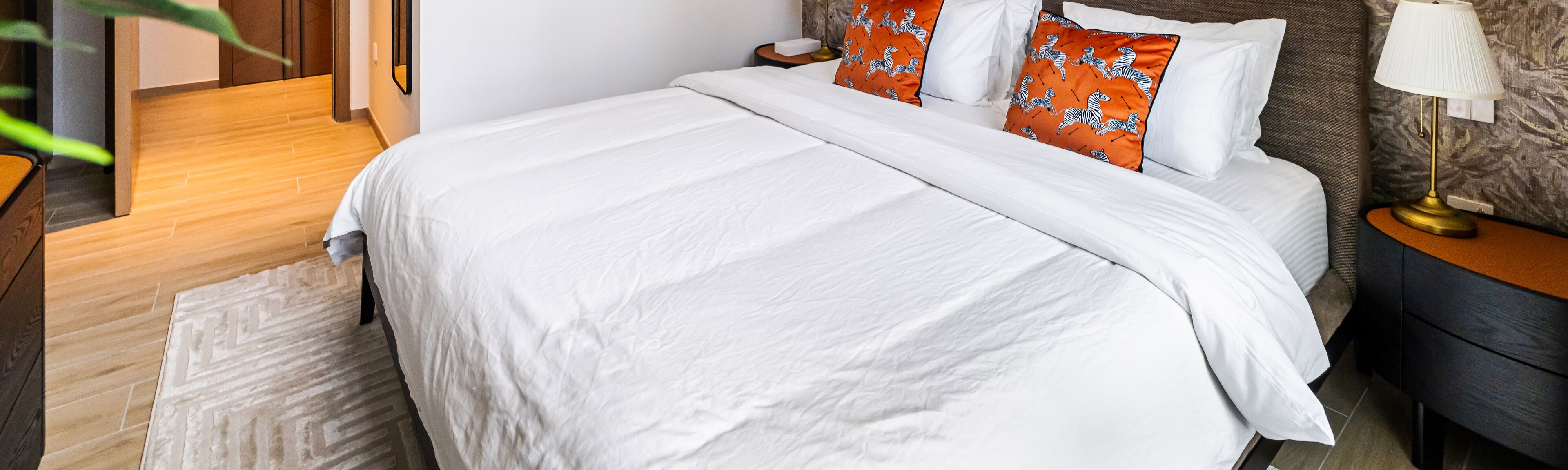 A neatly made bed with white bedding and two orange pillows with zebra prints.