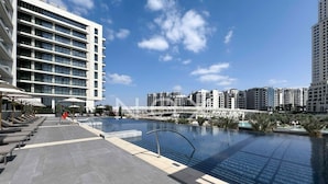 A modern hotel with a rooftop infinity pool, lounge chairs, and a view of the city skyline.
