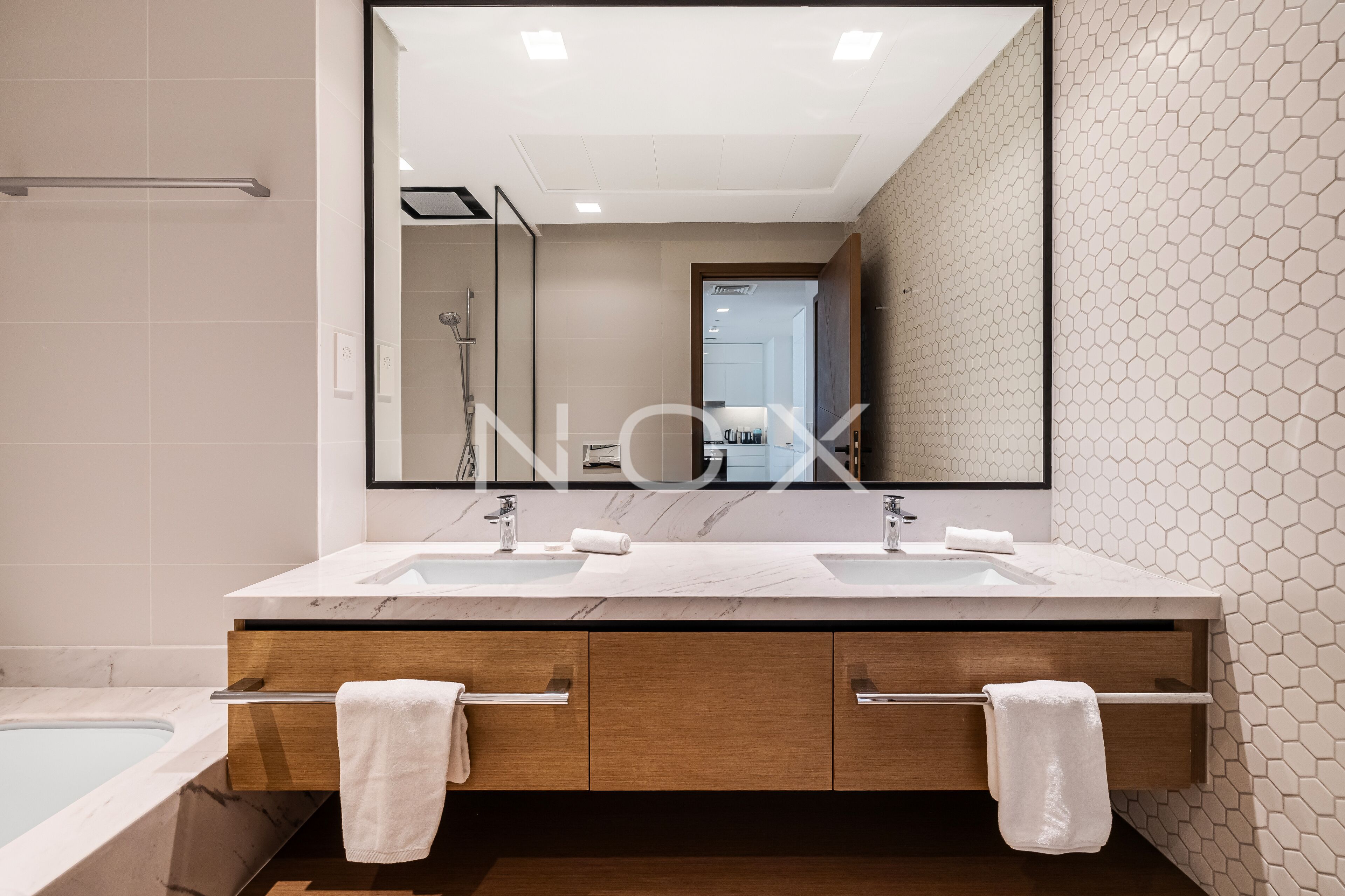 A modern bathroom with two sinks, a large mirror, and a bathtub.