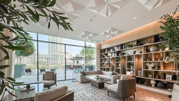 A modern living room with a large window, a geometric patterned floor, and a bookshelf filled with decorative items.
