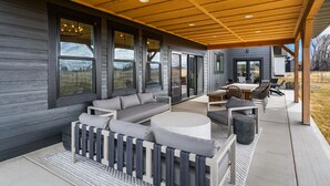 Eine überdachte Terrasse mit Holzboden, grau gepolsterten Sitzmöglichkeiten und einem Essbereich mit Gartenmöbeln.