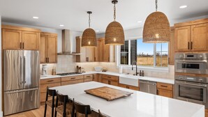 Eine moderne Küche mit Holzschränken, Edelstahlgeräten, einer großen Kochinsel mit Barhocker und Blick ins Freie.