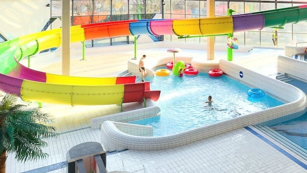 Un parque acuático interior con múltiples piscinas, toboganes y anillos hinchables.