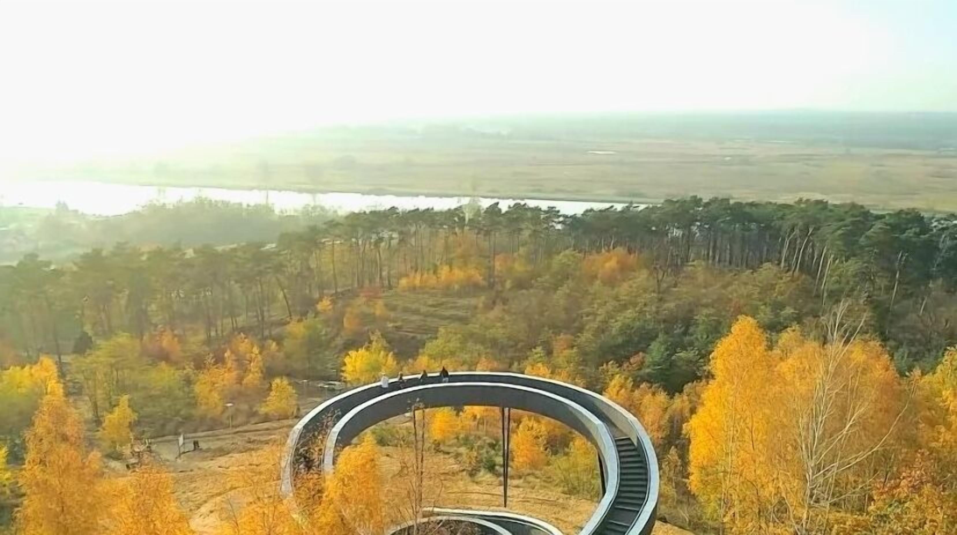 A circular road structure surrounded by autumn foliage and a distant river.