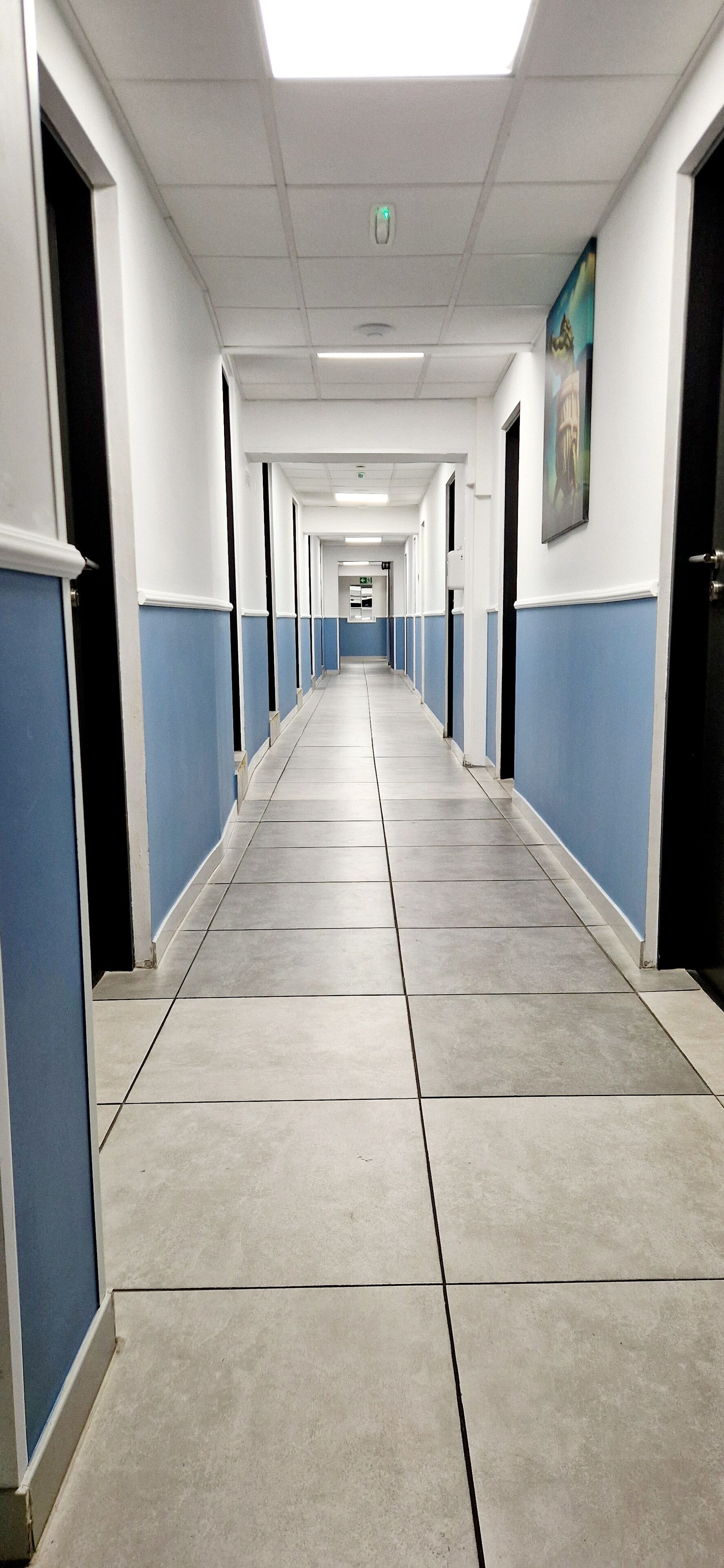 A long, narrow hallway with blue and white walls, tiled floors, and doors on both sides leading to rooms.