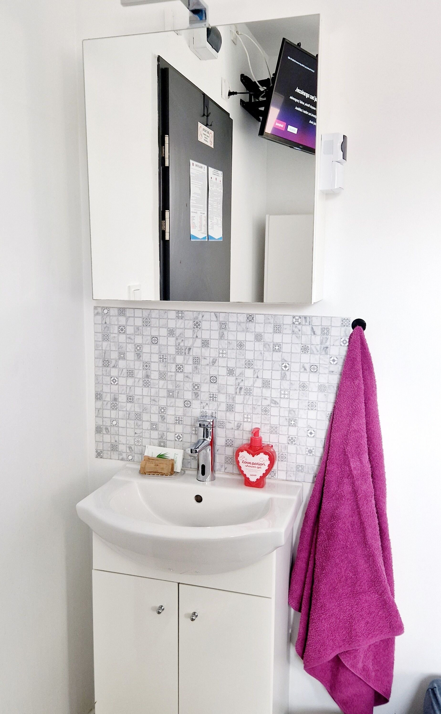 A bathroom with a white sink, a mirror, a tiled backsplash, and a pink towel hanging on a hook.