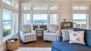 Ein geräumiges Wohnzimmer mit großen Fenstern, einem blauen Sofa, gestreiften Sesseln und einem kleinen runden Tisch.